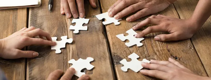 Hands connecting puzzle pieces on wooden table.