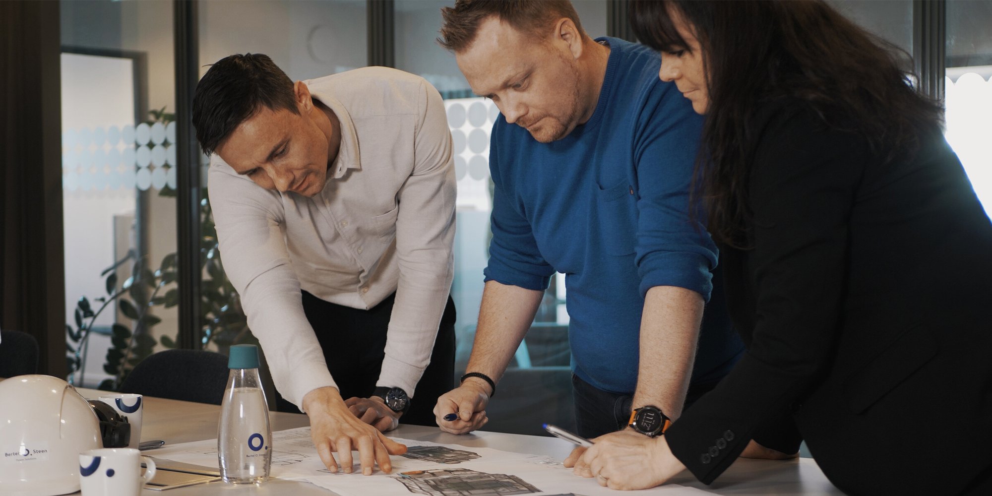 Kolmen henkilön ryhmä työskentelee yhdessä asiakirjojen parissa toimistossa. Kolmen henkilön ryhmä työskentelee yhdessä asiakirjojen parissa toimistossa.